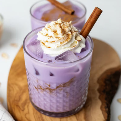 Purple iced ube latte topped with whipped cream, cinnamon stick and spices in a glass on wooden board Image